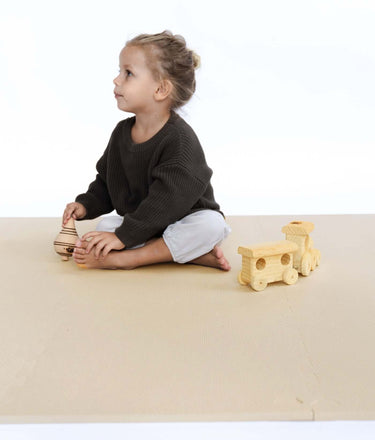 Toddler sitting sideways holding wooden toy on toddlekind baby toddler foam modern puzzle play mat classic clay.
