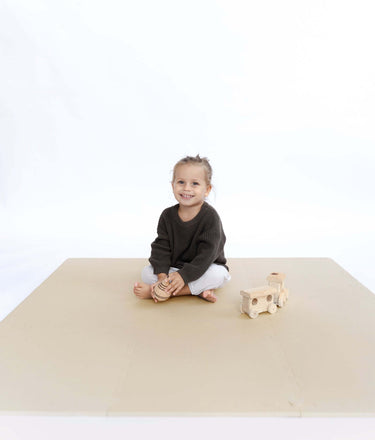Smiling toddler sitting on floor with wooden toy train on toddlekind baby toddler foam modern puzzle play mat classic clay.