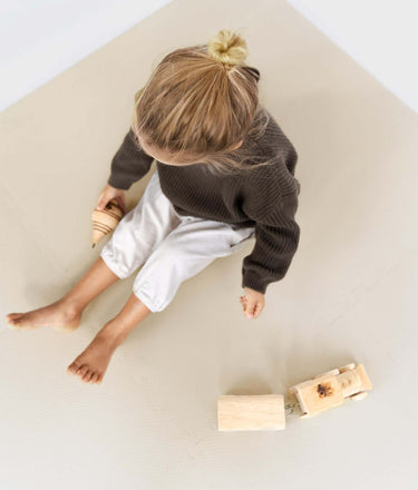 Top view of toddler sitting and playing with wooden toys on toddlekind baby toddler foam modern puzzle play mat classic clay.