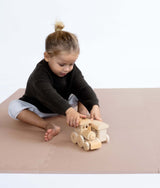 Toddler sitting and playing with wooden toy train on toddlekind baby toddler foam modern puzzle play mat classic blush.