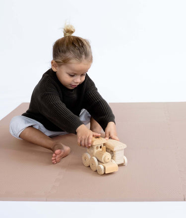 Toddler sitting and playing with wooden toy train on toddlekind baby toddler foam modern puzzle play mat classic blush.