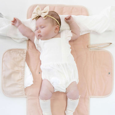 Baby lying comfortably on toddlekind baby portable changing clutch mini maven blush with quilted cushioning.
