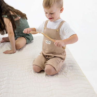 Toddler playing with wooden toy on soft quilted surface – toddlekind portable water resistant wander grande play mat tofu for sensory play
