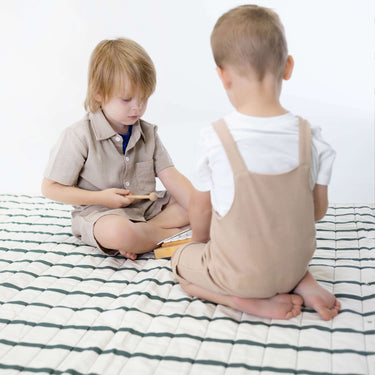 Two toddlers sitting and playing with wooden toy on padded striped mat – toddlekind portable water resistant wander grande play mat forest for shared playtime
