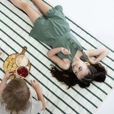 Child lying on striped play mat during indoor play – toddlekind portable water resistant wander grande play mat forest for comfort and relaxation
