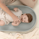 Parent changing baby on toddlekind baby foam changing pad nest pad sage with soft contoured support.

