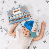 Overhead view of baby toddler lying down with a toy radio, enjoying the toddlekind baby toddler foam modern designer puzzle play mat haven amira seagrass
