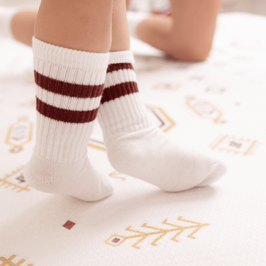 Close-up of baby toddler feet in striped socks standing on the toddlekind baby toddler foam modern designer puzzle play mat haven amira golden clay
