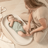 Parent caring for baby on toddlekind baby foam changing pad nest pad turtle dove in a cozy neutral setting.
