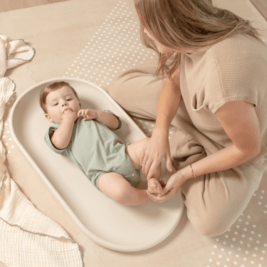Parent caring for baby on toddlekind baby foam changing pad nest pad turtle dove in a cozy neutral setting.
