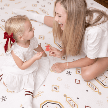Parent and baby toddler sitting together smiling and sharing a lollipop on the toddlekind baby toddler foam modern designer puzzle play mat haven amira golden clay.
