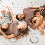 Parents and baby toddler lying on the mat smiling together, showcasing the toddlekind baby toddler foam modern designer puzzle play mat haven amira seagrass.
