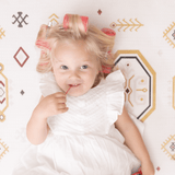 Baby toddler lying on the mat with hair rollers and holding a lollipop on the toddlekind baby toddler foam modern designer puzzle play mat haven amira golden clay.
