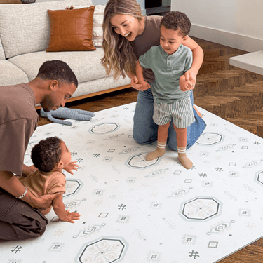 Family interacting with baby toddler on the floor in a cozy living room, highlighting the toddlekind baby toddler foam modern designer puzzle play mat haven amira seagrass.
