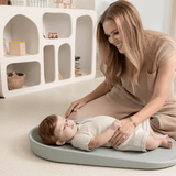 Smiling parent interacting with baby on toddlekind baby foam changing pad nest pad sage with ergonomic design.

