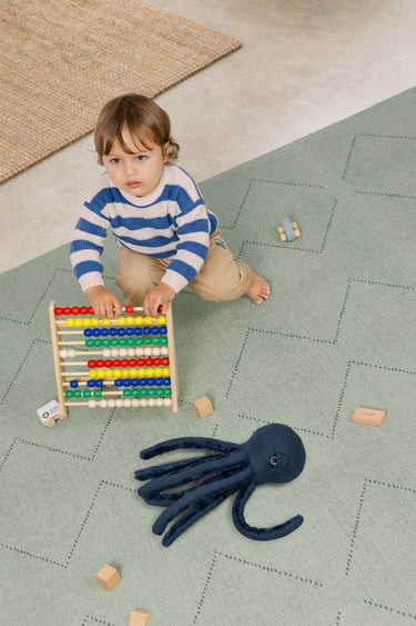 Child playing with an abacus and a toy octopus on a haven mat tulum agave