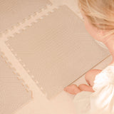 Person assembling interlocking tiles of the toddlekind baby toddler foam modern designer puzzle play mat haven deco latte on a light floor.
