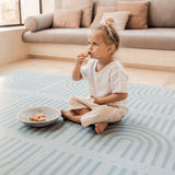Toddler sitting and eating a snack beside a bowl on the toddlekind baby toddler foam modern designer puzzle play mat haven linear mineral.
