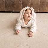 Baby in a white outfit crawling on the toddlekind baby toddler foam modern designer puzzle play mat haven tulum bone.

