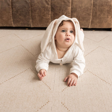 Baby in a white outfit crawling on the toddlekind baby toddler foam modern designer puzzle play mat haven tulum bone.
