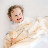 Smiling baby lying with toddlekind 3 layer cotton muslin baby blanket kind cloth sage draped softly over body.

