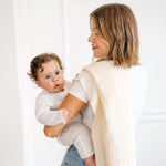 Parent holding baby wrapped in toddlekind 3 layer cotton muslin baby blanket kind cloth blush in a soft neutral setting.
