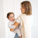 Parent holding baby wrapped in toddlekind 3 layer cotton muslin baby blanket kind cloth blush in a soft neutral setting.
