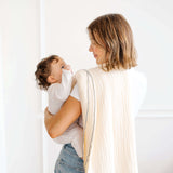 Parent holding baby wrapped in toddlekind 3 layer cotton muslin baby blanket kind cloth sage in a bright minimal home.
