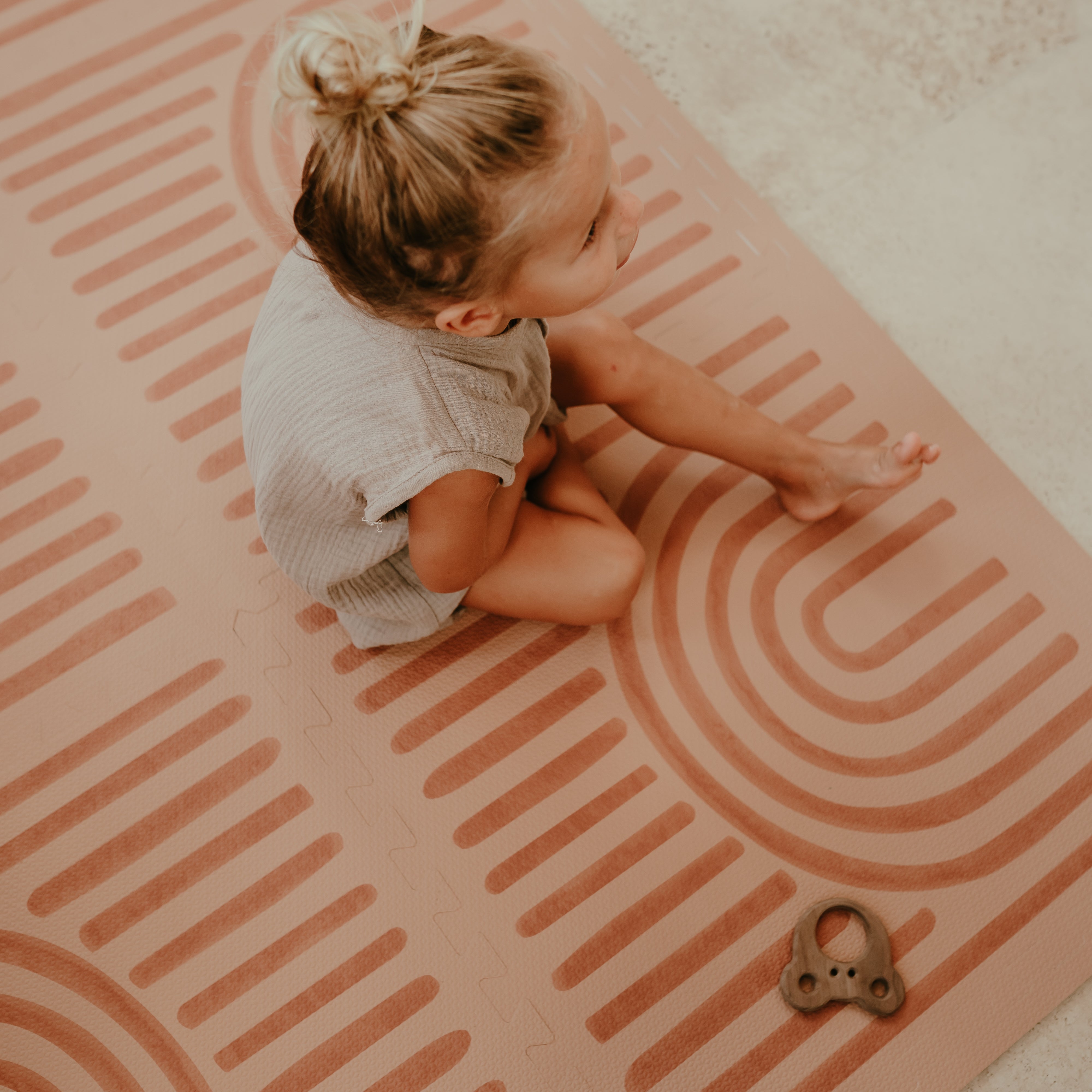 Baby toddler sitting on the patterned surface with a toy on the toddlekind baby toddler foam modern designer puzzle play mat haven linear camel.
