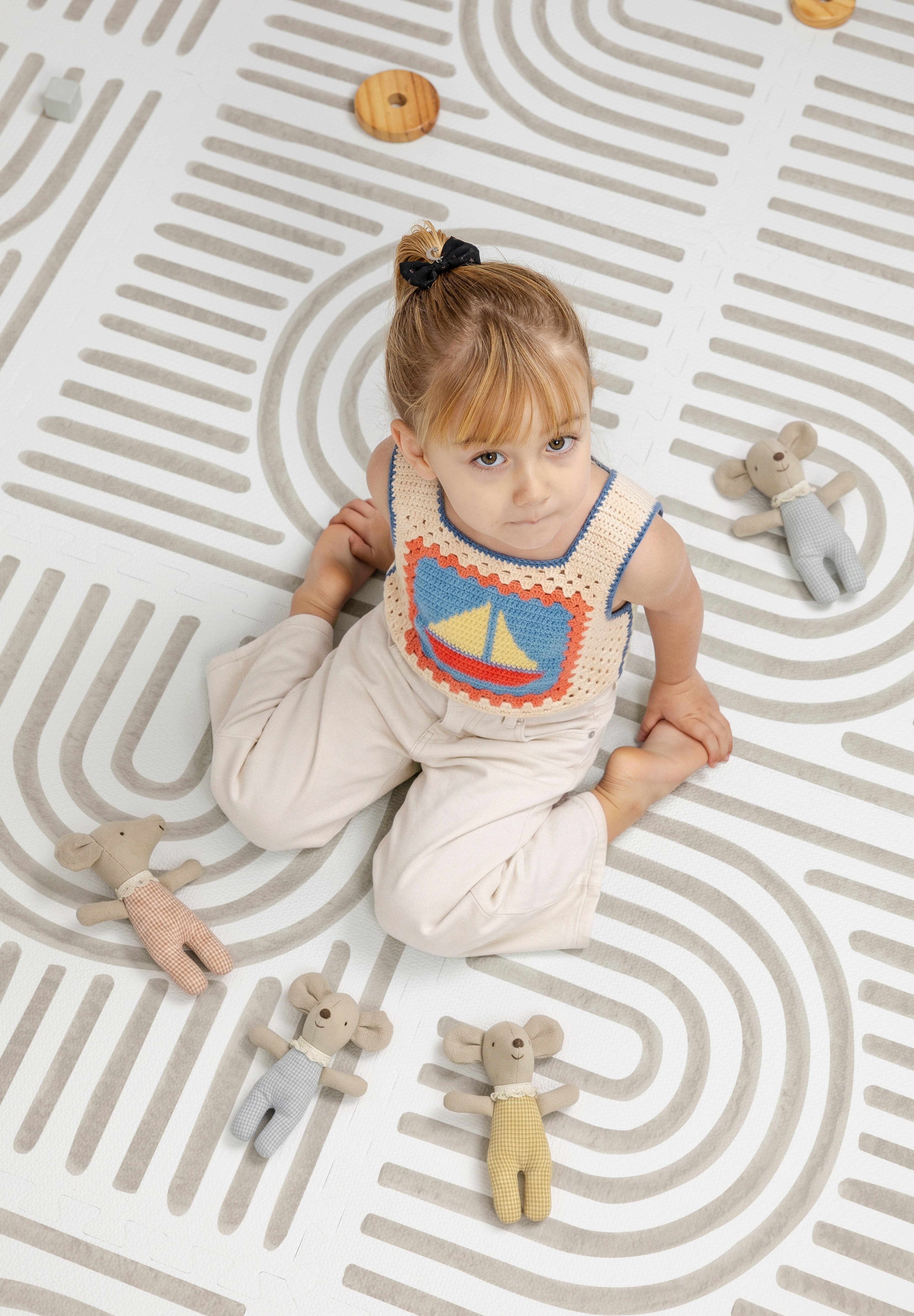 Child sitting on the Toddlekind Linear Putty foam playmat surrounded by soft toy mice.
