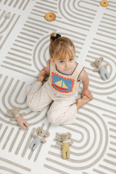 Child sitting on the Toddlekind Linear Putty foam playmat surrounded by soft toy mice.