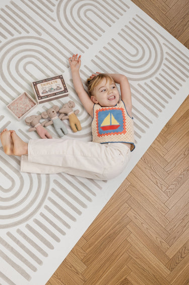 Child lying on the Toddlekind Linear Putty foam playmat showcasing the modern linear pattern.