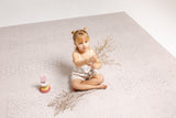 Child sitting on the haven mat surface with dried flowers and a toy.