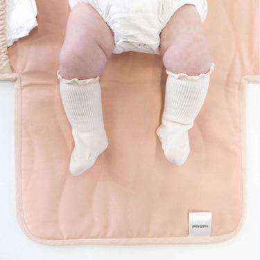 Close-up of baby legs on toddlekind baby portable changing clutch mini maven blush with soft padded surface.
