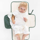 Baby resting on toddlekind baby portable changing clutch mini maven forest with side pockets and soft padding.
