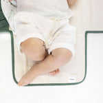 Close-up of baby legs on toddlekind baby portable changing clutch mini maven forest with soft cushioned interior.
