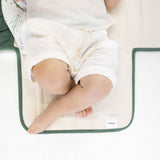 Close-up of baby legs on toddlekind baby portable changing clutch mini maven forest with soft cushioned interior.

