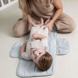 Parent changing toddler on toddlekind baby portable changing clutch mini maven slate with supportive padded design.
