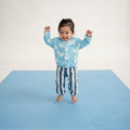 Smiling toddler standing with arms raised on toddlekind baby toddler foam modern puzzle play mat classic slate.
