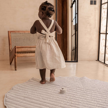 Toddler standing and exploring on organic cotton padded baby toddler toddlekind play mat tummy time quilted snuggle mat stone stripes near window light.
