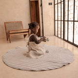 Toddler playing on organic cotton padded baby toddler toddlekind play mat tummy time quilted snuggle mat stone stripes in a bright minimal room.
