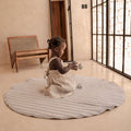 Toddler playing on organic cotton padded baby toddler toddlekind play mat tummy time quilted snuggle mat stone stripes in a bright minimal room.

