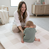 Mother and toddler sitting together on toddlekind baby toddler foldable foam cushioned tumble play mat arden dove in cozy home setting.
