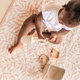 Toddler reaching into bucket while seated on patterned mat – toddlekind portable water resistant wander classic play mat ocean sea shell for easy-clean activities
