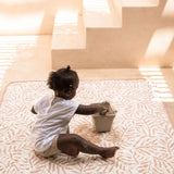 Toddler sitting on soft mat with bucket and sand toys indoors – toddlekind portable water resistant wander classic play mat ocean sea shell for everyday play
