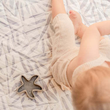 Close-up of baby legs and toy on soft patterned mat – toddlekind portable water resistant wander classic play mat ocean stone with gentle padding
