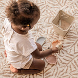 Baby playing with sand toys on leaf-pattern mat indoors – toddlekind portable water resistant wander classic play mat ocean tan for sensory play
