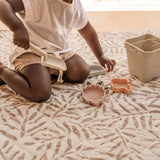 Close-up of toddler scooping sand with toys on cushioned mat – toddlekind portable water resistant wander classic play mat ocean tan for mess-free play
