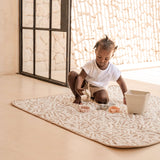Child sitting on patterned mat with toys near open doorway – toddlekind portable water resistant wander classic play mat ocean tan for versatile play areas
