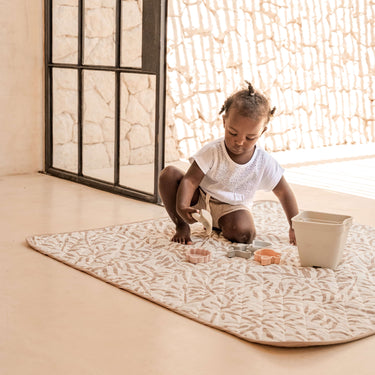 Child sitting on patterned mat with toys near open doorway – toddlekind portable water resistant wander classic play mat ocean tan for versatile play areas

